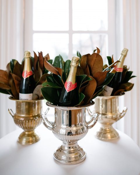 Elegant silver trophy cups filled with champagne bottles and decorative leaves, displayed on a white.