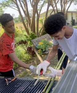Young men using tools to tend to the farm's outdoor equipment and crops.