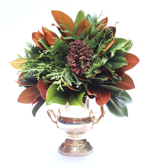 Elegant holiday floral arrangement with pinecones in a silver vase, featuring lush green and brown f.
