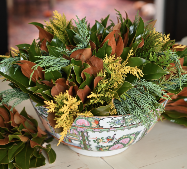 Festive floral arrangement with greenery and brown leaves in a decorative bowl.
