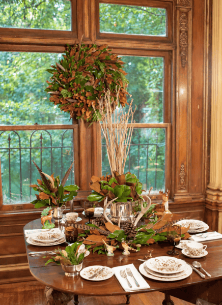 Elegant fall-themed wreath centerpiece on a dining table with greenery and natural accents.