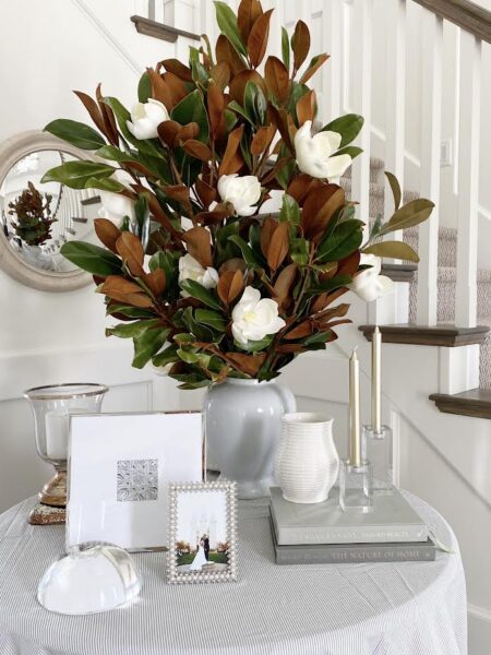 Elegant floral arrangement with white magnolia flowers and lush green and brown leaves in a white va.