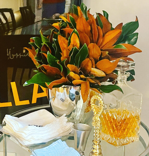 Elegant floral arrangement with orange and green leaves in a silver vase, accompanied by a glass dec.