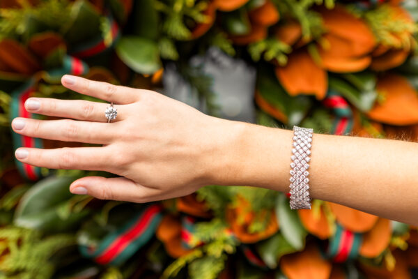 Close-up of a woman's hand showcasing a sparkling diamond ring and a silver bracelet, set against a.