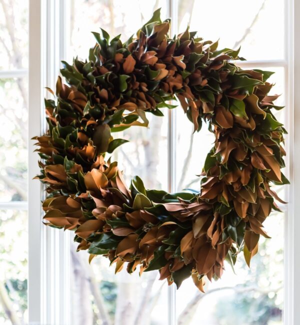 Wreath made of magnolia leaves hanging in front of a window.