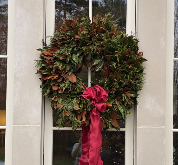 Festive holiday wreath with greenery and red ribbon on door.