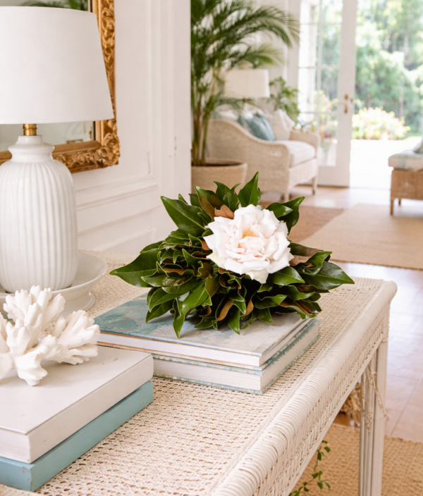 Elegant floral arrangement with white flowers and green leaves on a woven table in a bright, airy li.