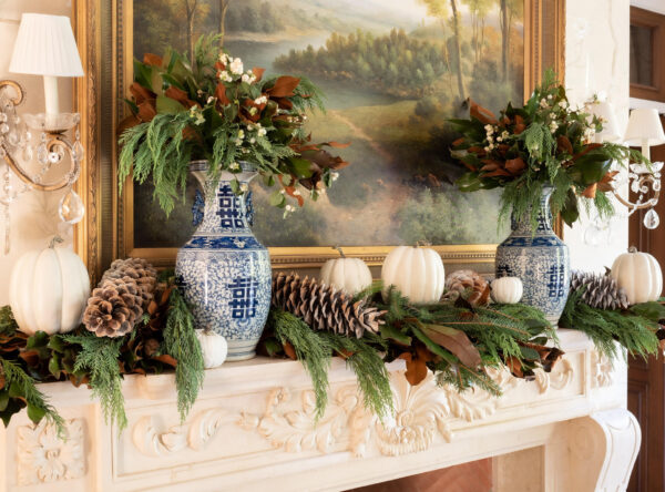 Elegant fireplace mantel decorated with blue and white vases, pinecones, pumpkins, and greenery for.