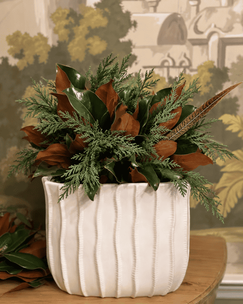 Elegant floral arrangement with greenery and brown leaves in a white ceramic vase.