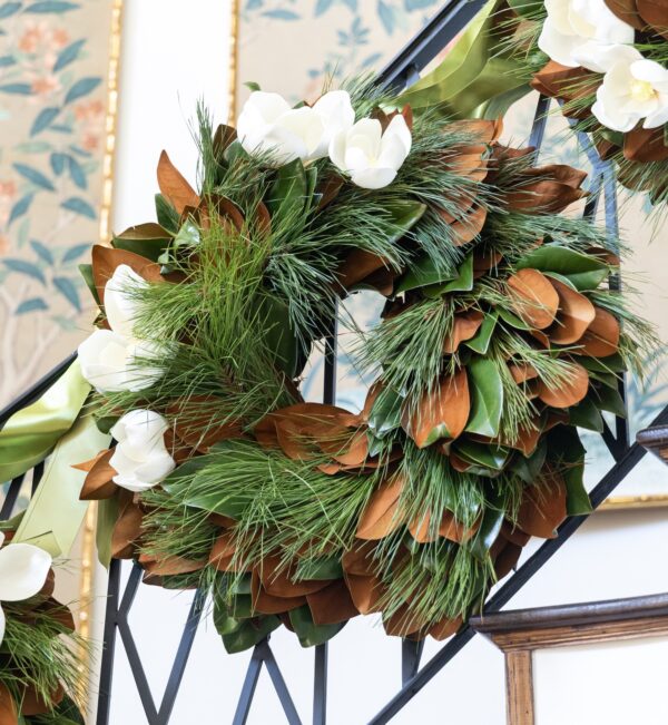 White and brown floral wreath with green foliage, displayed on a black metal stand indoors.