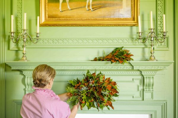 Woman arranging a fall-themed bouquet in front of a green fireplace mantel.