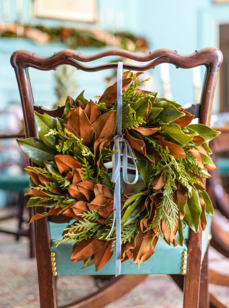 Brooke's Bank Emerald Lace 14" wreath with green and brown foliage on a wooden chair.