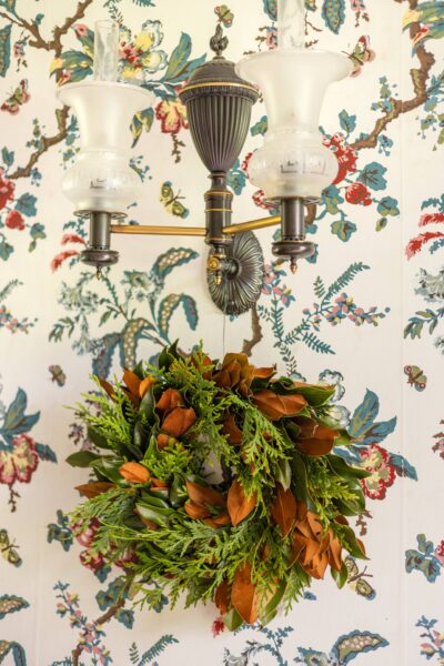 Vintage wall sconce with floral wreath hanging below, floral wallpaper background.