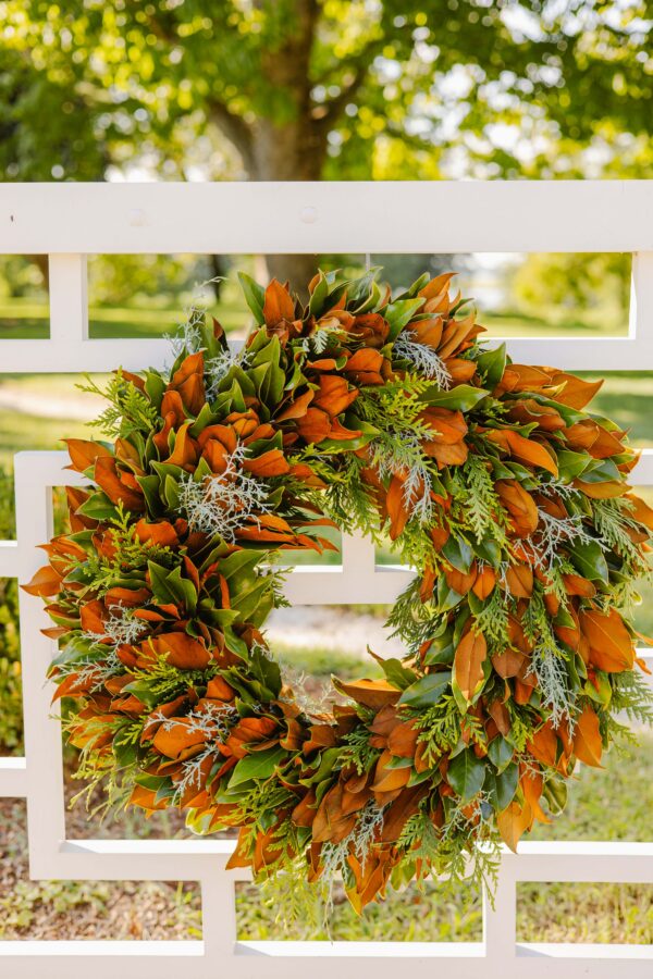 Autumn wreath with orange and green foliage hanging on a white fence.