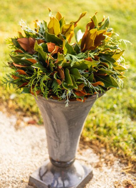 Elegant floral arrangement in a tall vase with greenery and brown accents.