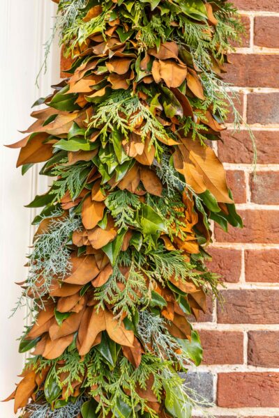 Festive greenery garland with leaves and pinecones on brick wall.