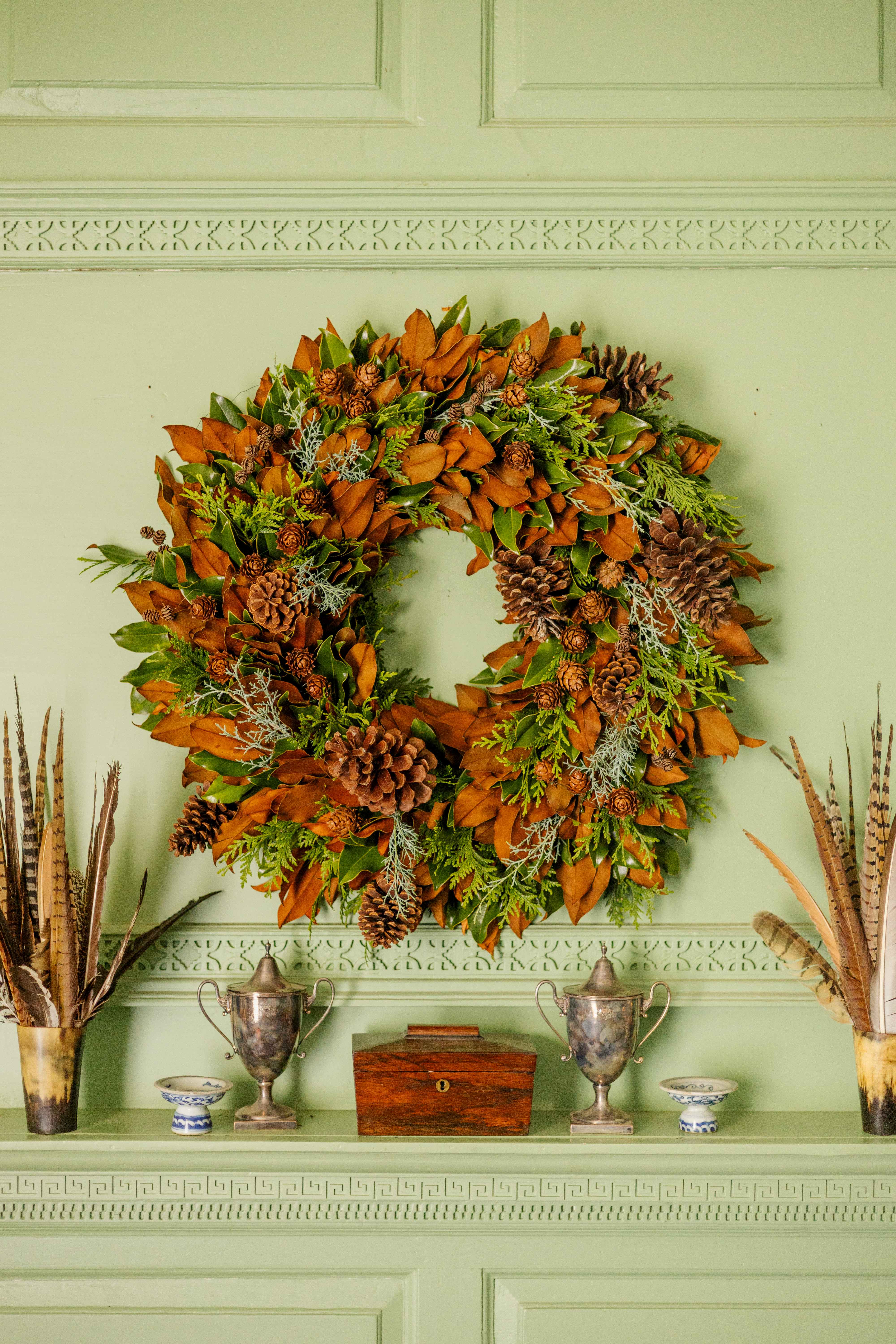 Brooke’s Bank wreath with magnolia foliage, conifers, and pinecones against historic green paneling.
